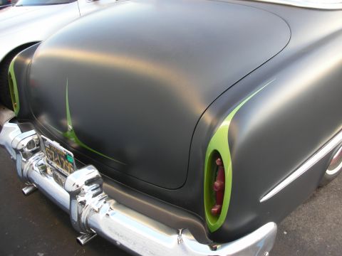 1998 Ford Crown Victoria - The rear of a customized classic car features a matte black finish with vibrant green accents and a chrome bumper.