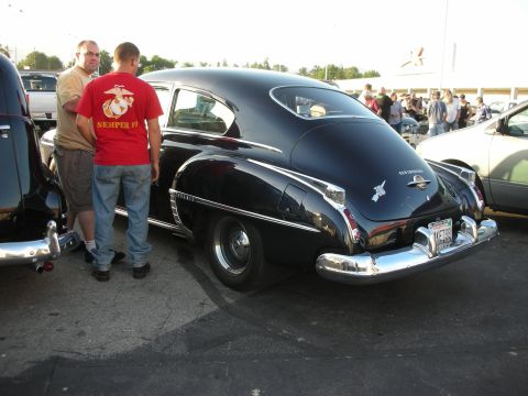 1998 Ford Crown Victoria - A black sedan with distinctive chrome accents is parked outdoors, with people milling around in the background.