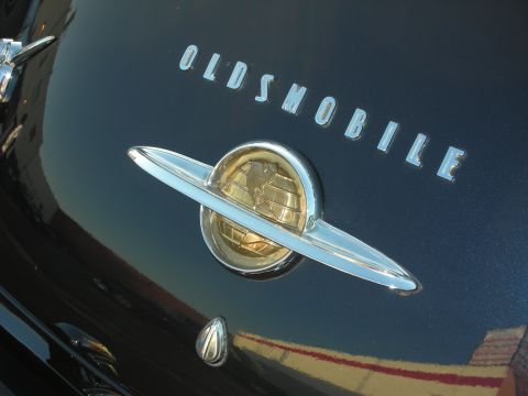 1998 Ford Crown Victoria - The chrome Oldsmobile emblem with a globe design is visible on the car's dark body.