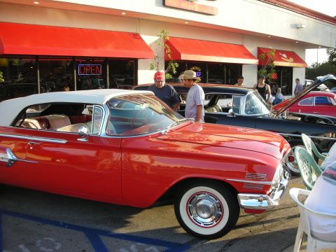 1998 Ford Crown Victoria - A group of people admire classic cars parked outside a building with red awnings.