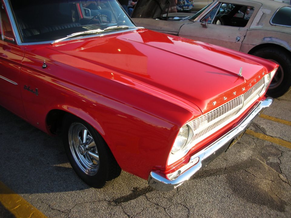 Red 1965 Plymouth Barracuda front quarter panel and grille. Another car is visible behind it