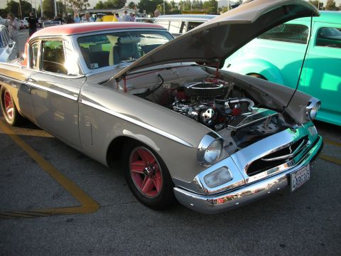 1998 Ford Crown Victoria - A classic Studebaker Hawk is displayed with its hood open, revealing the engine bay, next to another vintage car.