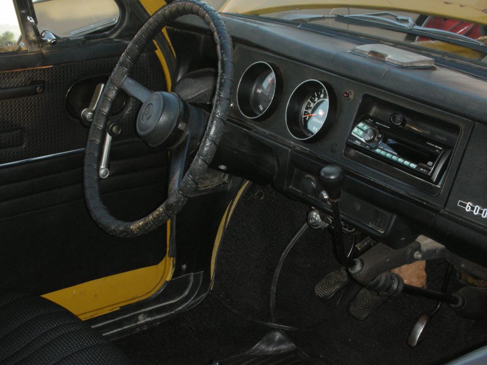 Interior view of a yellow car, showing the steering wheel, dashboard with gauges, radio, and gear shifter
