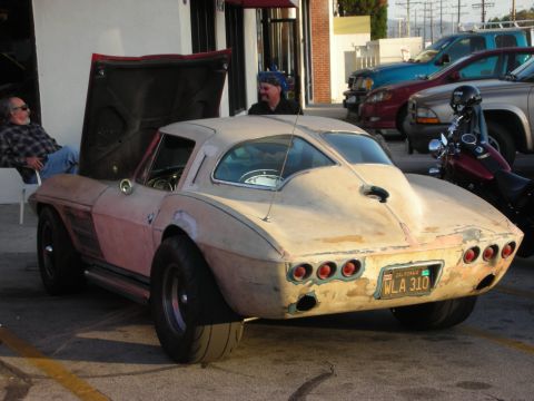 1998 Ford Crown Victoria - A beige primer Corvette Stingray with its hood open sits parked, showing its distinctive rear end and wide tires.