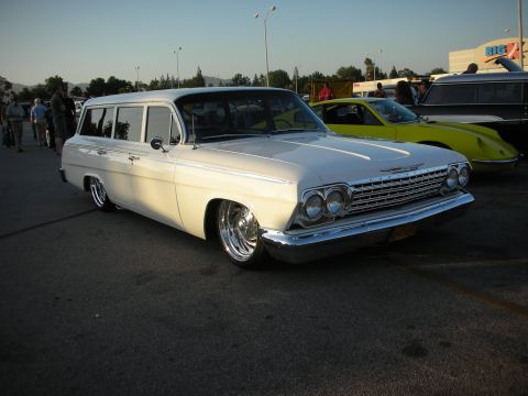 1998 Ford Crown Victoria - A classic white 1962 Chevrolet station wagon sits low on chrome wheels at an outdoor car show.