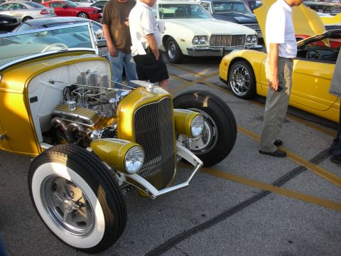 1998 Ford Crown Victoria - A yellow hot rod is parked next to other vehicles, including a yellow sports car.