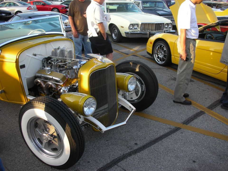 Yellow hot rod with exposed engine, chrome grille, and whitewall tires