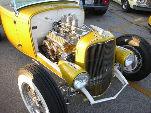 1998 Ford Crown Victoria - A bright yellow hot rod is displayed with its engine exposed, chrome details and triple carburetors.