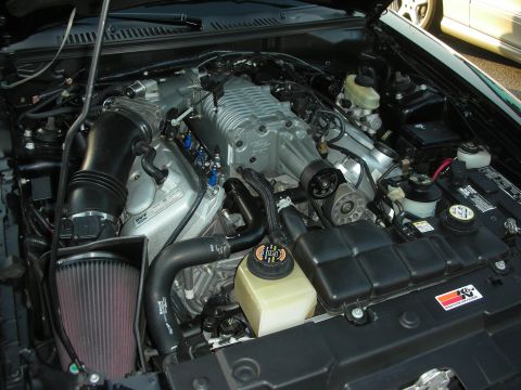 1998 Ford Crown Victoria - The engine bay of a car, showing a supercharger and other components, with another vehicle in the background.