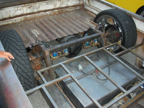 1998 Ford Crown Victoria - The bed of a truck shows custom air suspension components and a fuel tank, with a yellow vehicle visible in the background.