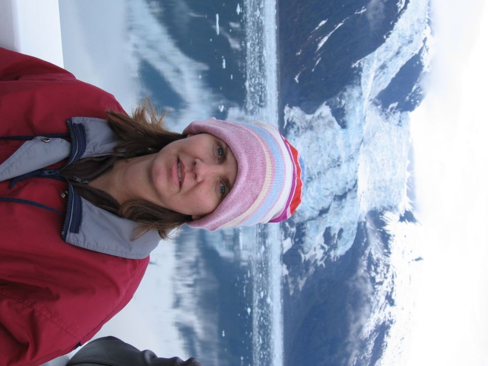 Woman in red jacket and striped hat with glacier in background