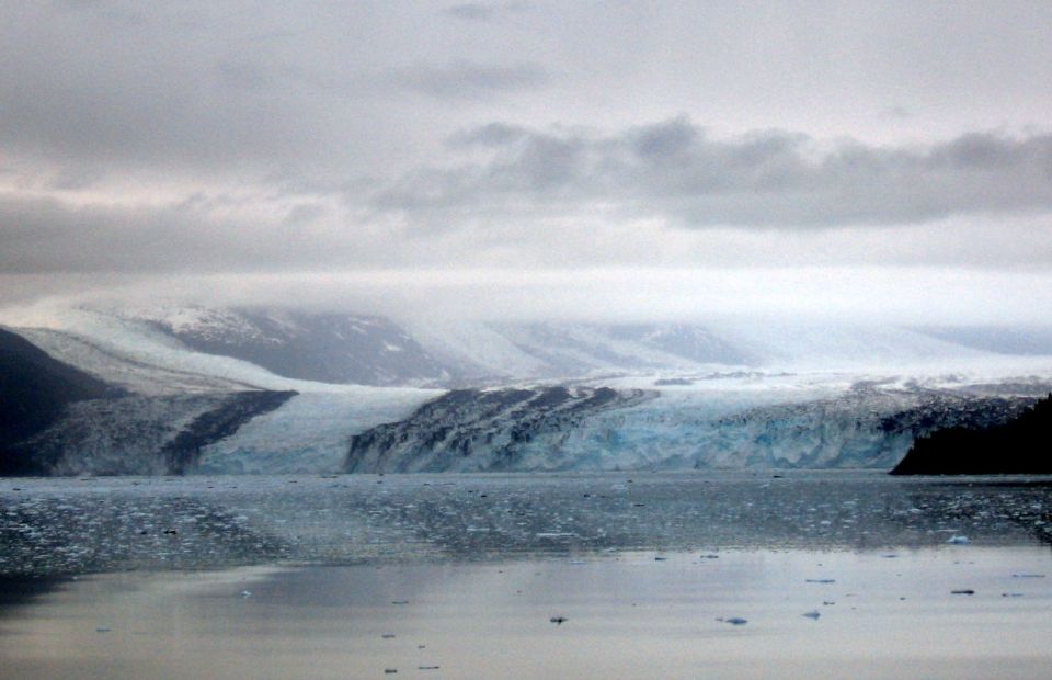 Glacier calving into the ocean under a cloudy sky