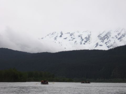 1973 Ford Ranchero - People enjoy a rafting trip on a river with a backdrop of snow-covered mountains and dense forests.