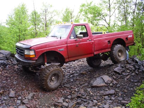 1994 Ford F-250 - This red 1994 Ford F-250 pickup truck navigates a challenging rocky path, its lifted suspension and off-road capabilities.