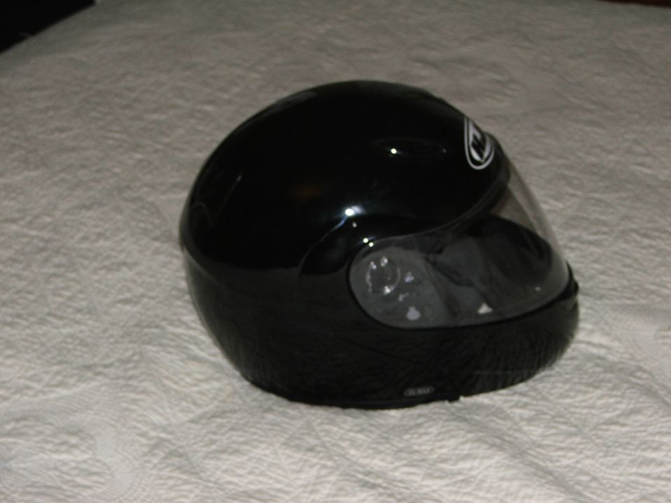 Gloss black full-face motorcycle helmet with clear visor on a white bedspread