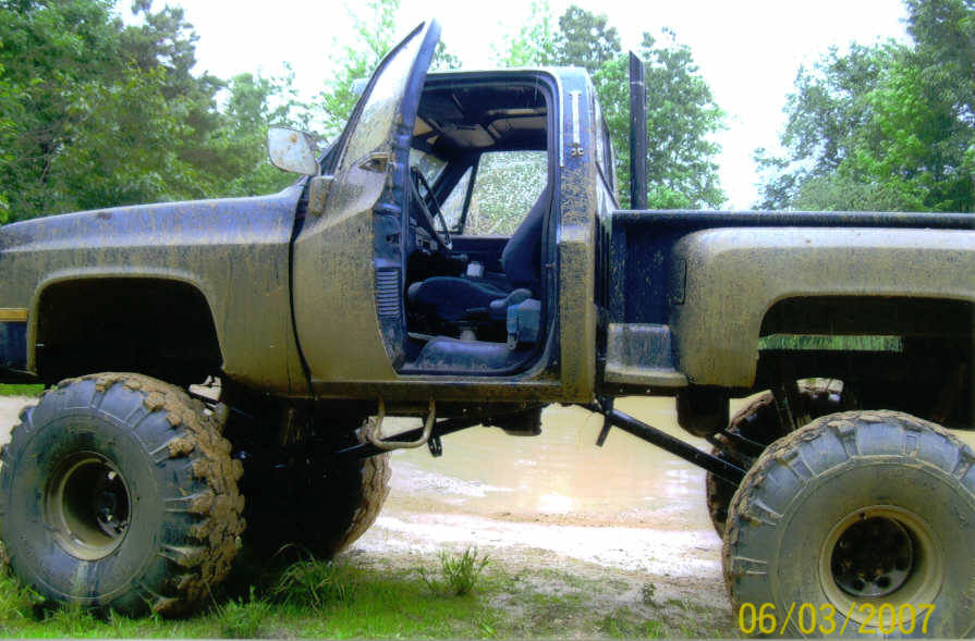 Mud-covered pickup truck with lifted suspension and oversized tires, driver's door open