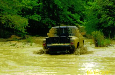 1976 Chevrolet Blazer - Pickup truck navigating through a muddy, water-filled area with trees in the background.