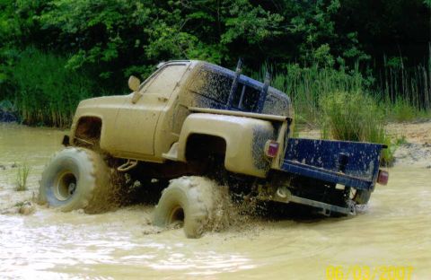 1976 Chevrolet Blazer - This lifted truck is deep in the mud, kicking up water as it drives through a swampy area.