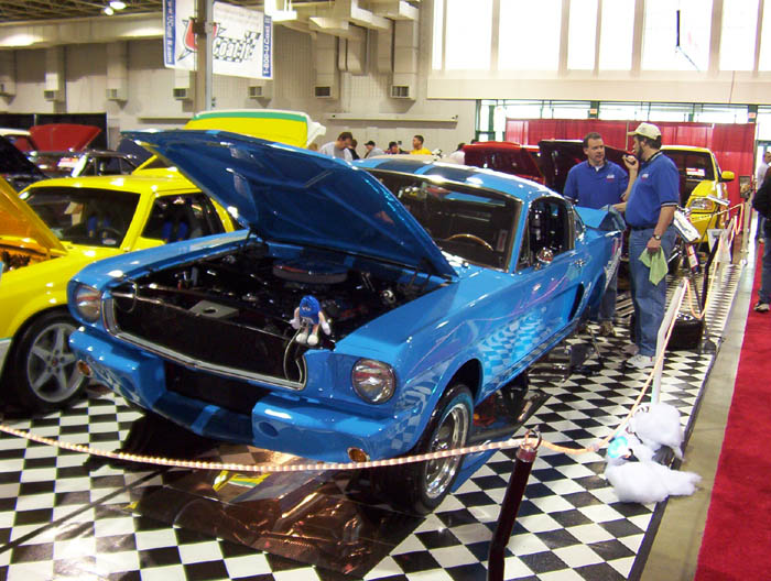 Blue classic Mustang fastback with hood raised at indoor car show on checkered floor