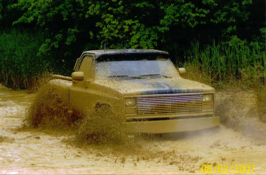 Mud-splattered 1975 pickup truck driving through water, front view