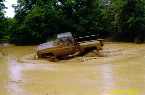 1976 Chevrolet Blazer - This pickup truck is stuck deep in the mud and water, with trees visible behind it.