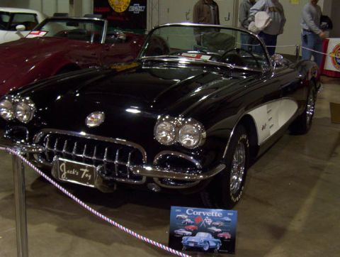 1993 Ford Taurus - A black 1958 Chevrolet Corvette convertible is displayed indoors with other vehicles and promotional material.