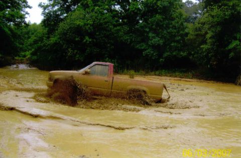 1976 Chevrolet Blazer - A pickup truck is stuck in a muddy area, with trees in the background.