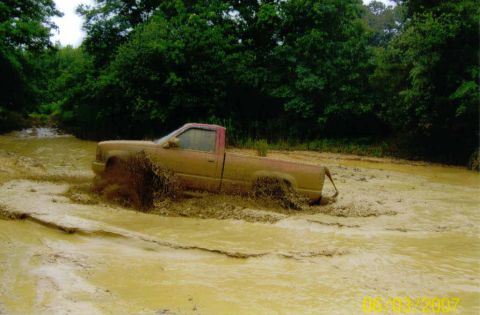 1976 Chevrolet Blazer - A truck navigates a challenging muddy terrain, kicking up significant spray.