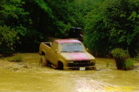 1976 Chevrolet Blazer - A pickup truck is stuck in a muddy water crossing, with another vehicle visible in the background.