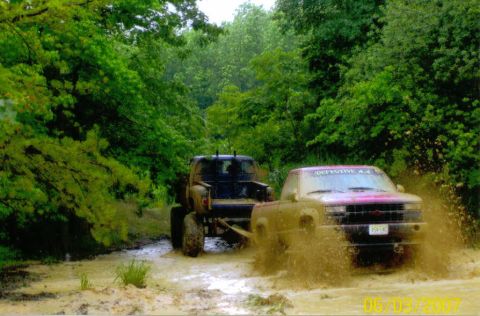 1976 Chevrolet Blazer - Off-roading adventure: two trucks tackle a challenging muddy trail surrounded by lush greenery.