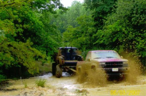 1976 Chevrolet Blazer - Off-road trucks navigate a muddy path, sending water and dirt flying.