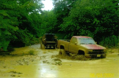 1976 Chevrolet Blazer - Two trucks navigate a muddy trail, with the lead vehicle partially submerged in the muck.