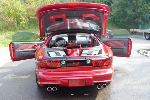 1993 Pontiac Firebird - Rear view of a red 1993 Pontiac Firebird, its open doors and trunk revealing a custom interior with audio equipment.