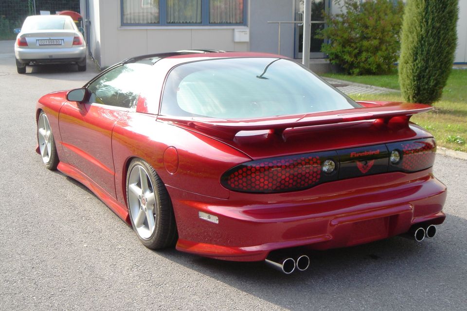 Candy red Pontiac Firebird coupe rear view with body kit, custom taillights, dual exhaust and polished wheels
