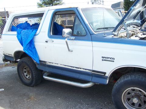 1991 Ford Bronco - A white and blue Ford Bronco is parked outdoors with its hood open and a blue tarp covering part of the interior.