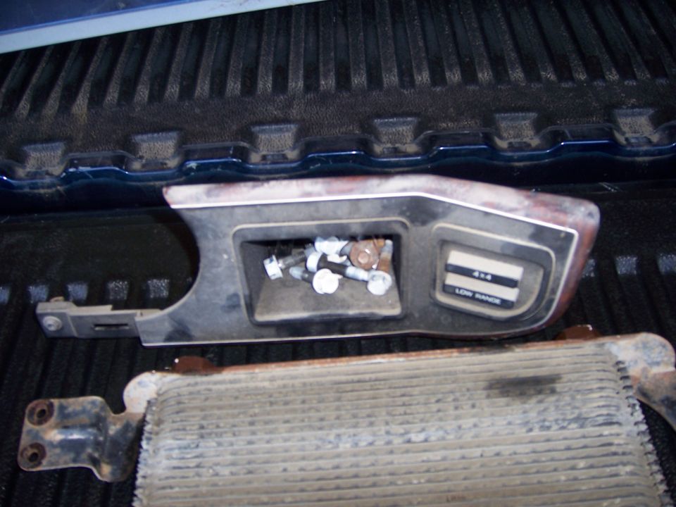 4x4 shifter trim with '4x4' and 'LOW RANGE' labels, holding bolts, next to an oil cooler