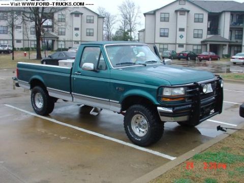 1996 Ford F-150 - A green 1996 Ford F-150 pickup truck is parked in a lot with apartment buildings in the background.