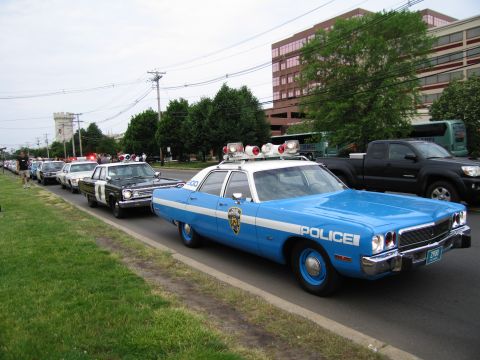 1991 Ford LTD Crown Victoria - light-blue 1970s NYPD four-door cruiser with roof lightbar sits at the front of a row of classic police cars on a grassy roadside.
