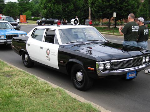 1991 Ford LTD Crown Victoria - black-and-white classic LAPD-marked police sedan with twin roof spotlights and siren is parked roadside as bystanders look on.