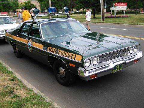 1991 Ford LTD Crown Victoria - dark-green 1970s State Trooper sedan with a gold body stripe and twin roof spotlights is parked along a grassy curb.