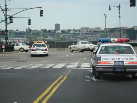 1991 Ford LTD Crown Victoria - North Haven Police cruiser sits at a wide intersection with other police cars and a city skyline in the hazy background.