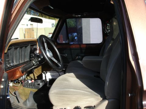 1977 Ford F-150 - The interior of a vintage truck features a wood-grain dashboard, a three-spoke steering wheel, and cloth bucket seats.