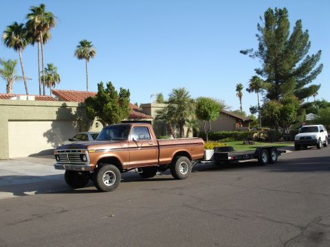 1977 Ford F-150 - Brown 1977 Ford F-150 pickup truck is seen towing a trailer on a sunny day.