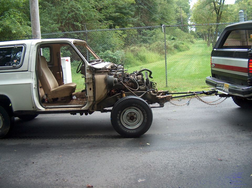 Stripped white square-body truck cab with no front clip being tow-barred behind a green Bronco