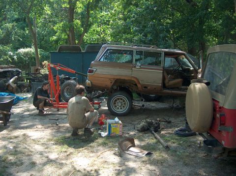 1996 Ford F-250 - A Jeep Grand Wagoneer is undergoing repairs outdoors, with parts and tools scattered around.