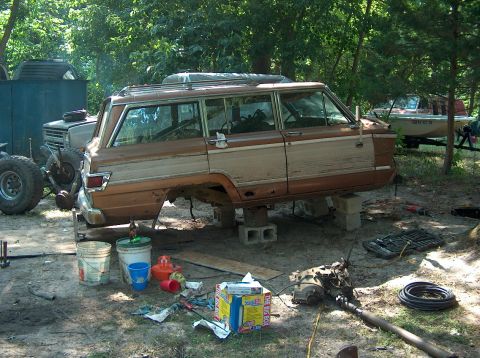 1996 Ford F-250 - A disassembled Jeep Grand Wagoneer sits outdoors, surrounded by parts and tools, awaiting repair.