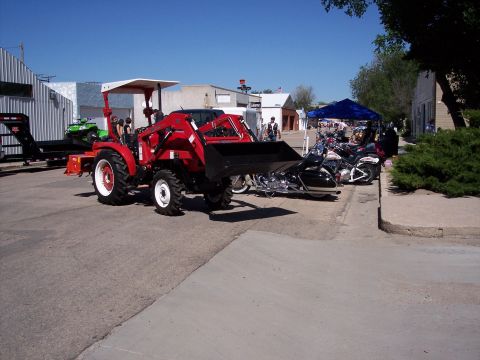 1972 Ford Ranchero - A red tractor with a front loader is parked on a street next to several motorcycles and a trailer.