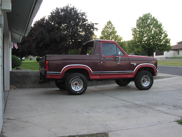 Side view of maroon 1981 Ford Bronco with rear top removed, red lower panels, white-letter tires, parked on driveway