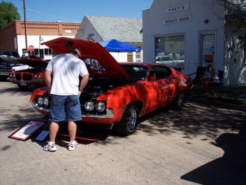 1972 Ford Ranchero - A man inspects the engine of a red coupe at an outdoor car show. Another vehicle is visible behind it.