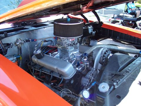 1972 Ford Ranchero - The engine bay of an orange vehicle is shown, with a motorcycle visible in the background.